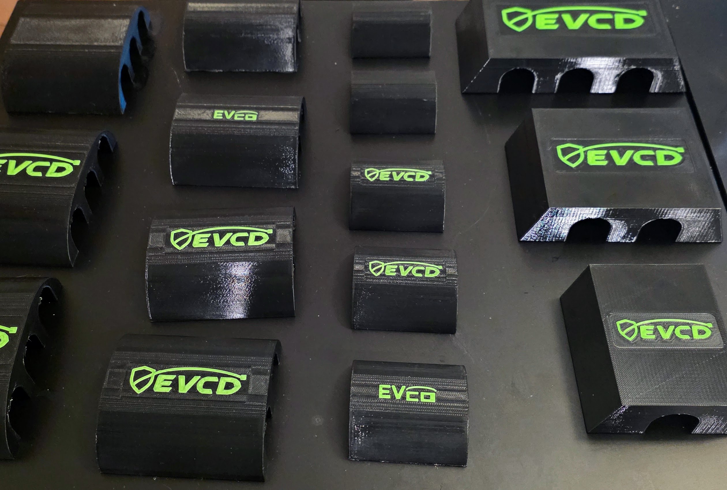 Real black-and-green EVCD Solo, Duo, and Trio guards arranged with an EV charging cable